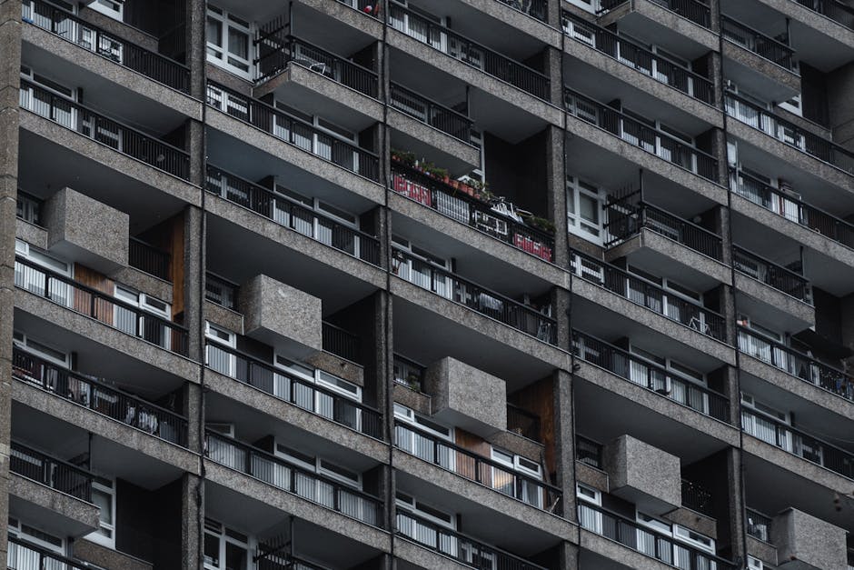 Close-up view of the exterior façade of a red-brick residential building on Heygate Estate, featuring multiple white-framed double-glazed windows arranged in a curved pattern, with some windows parti